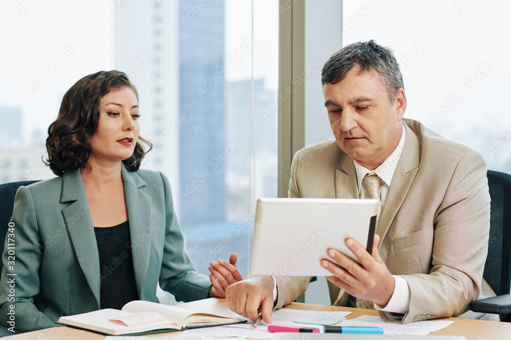 Middle-aged Caucasian man and mature woman working together sitting together at office desk, horizontal shot Middle-aged Caucasian man and mature woman working together sitting together at office desk, horizontal shot