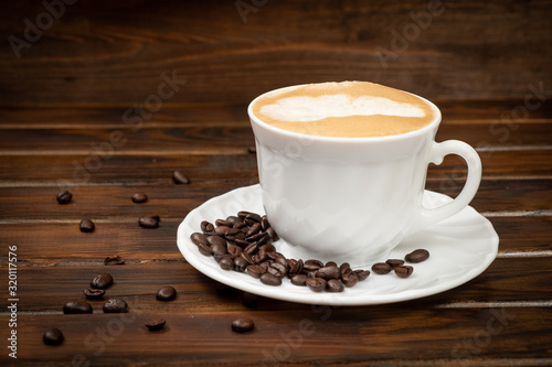 Cappuccino in a white glass on a saucer. Coffee beans on a saucer. Brown background