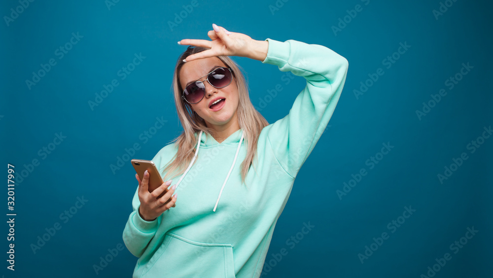 Stylish trendy hipster girl in the blue hoodie with the hood uses a smartphone. Stylish trendy hipster girl in the blue hoodie with the hood uses a smartphone.
