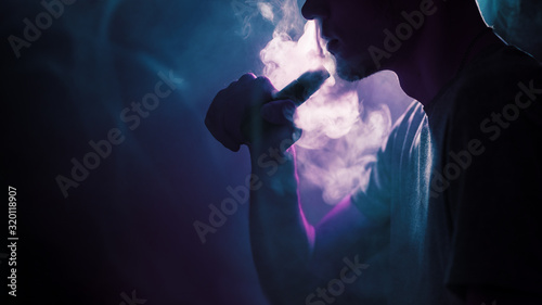 Close - up of a young man exhaling a cloud of steam or smoke using an electronic cigarette. Mechanical vaping mod .