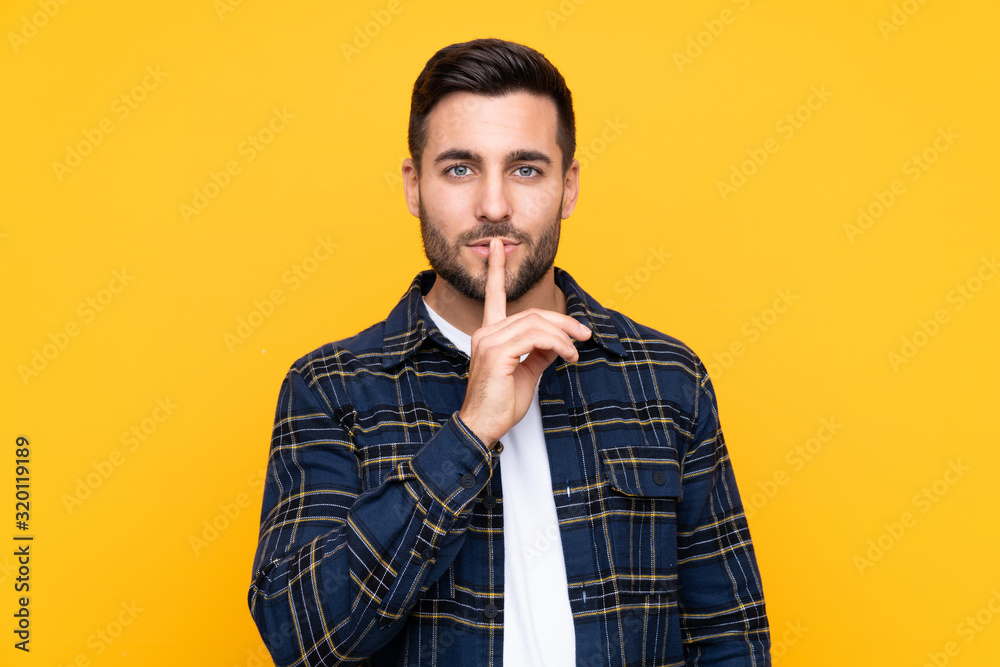 Young handsome man with beard over isolated yellow background showing a sign of silence gesture putting finger in mouth Young handsome man with beard over isolated yellow background showing a sign of silence gesture putting finger in mouth
