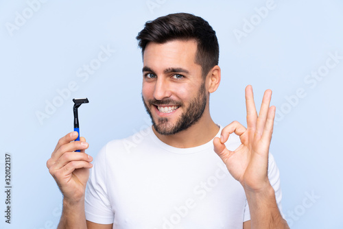 Young handsome man shaving his beard over isolated background showing ok sign with fingers