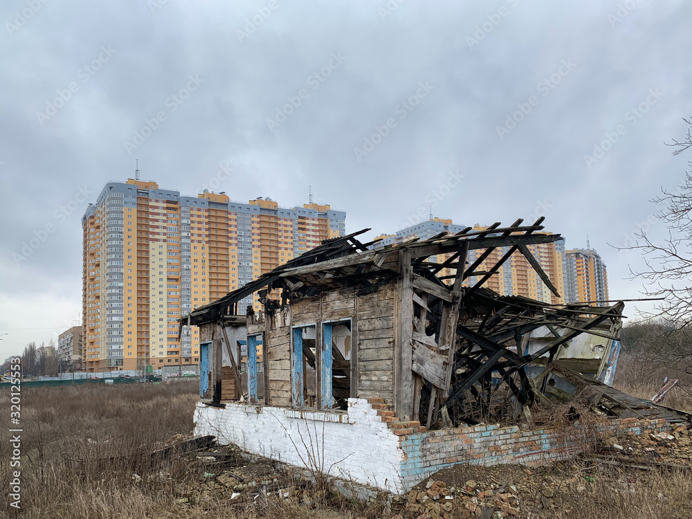 Old ruined house on the background of a new high-rise building. Abandoned house with no doors and windows with a broken roof. Concept: devastation, construction