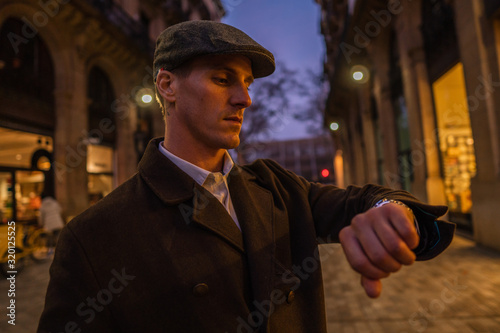 Old Fashion Man from the 1920s england walking along an old street of a historic city. He is checking time on wristwatch