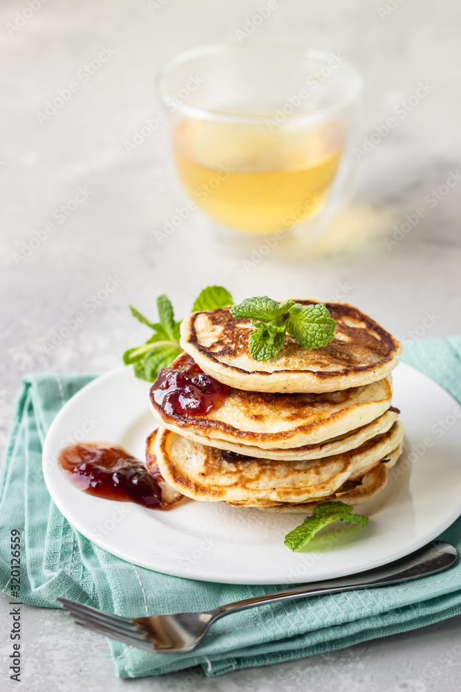 Pancakes with red berry jam and mint, herbal tea. American cuisine. Perfect idea for breakfast. Light grey stone background.