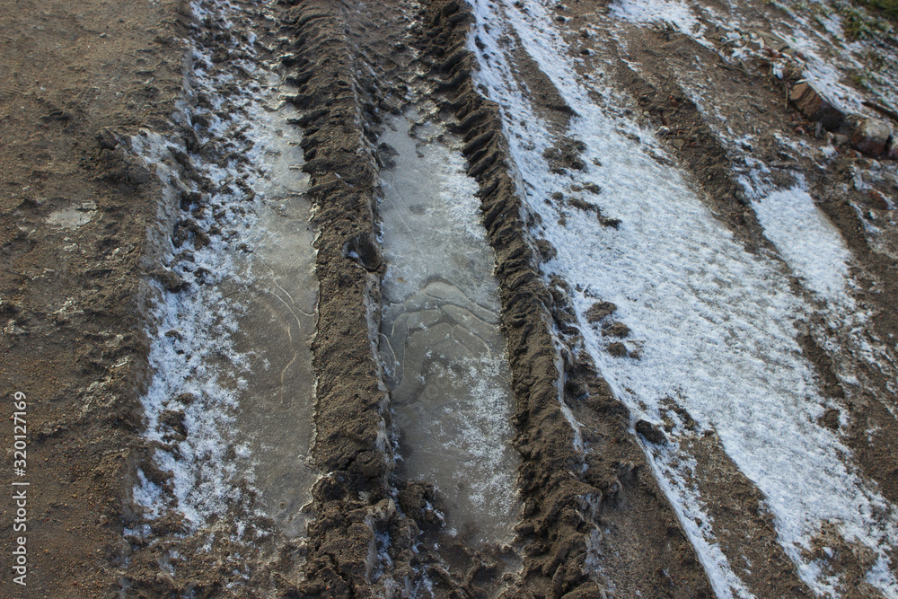 Bad road without asphalt, dirt, frost, ice crust on the ground, car tracks Bad road without asphalt, dirt, frost, ice crust on the ground, car tracks