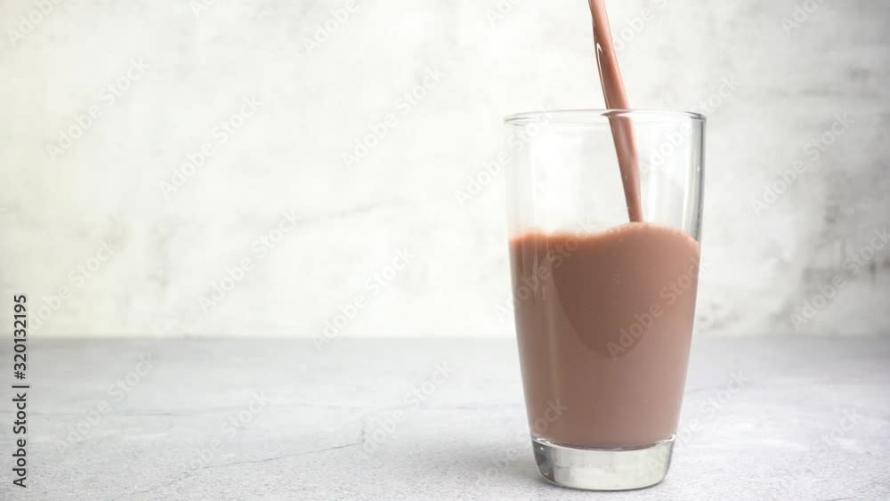 Close up pouring chocolate milk into a glass on the table.
