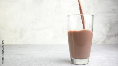 Close up pouring chocolate milk into a glass on the table.