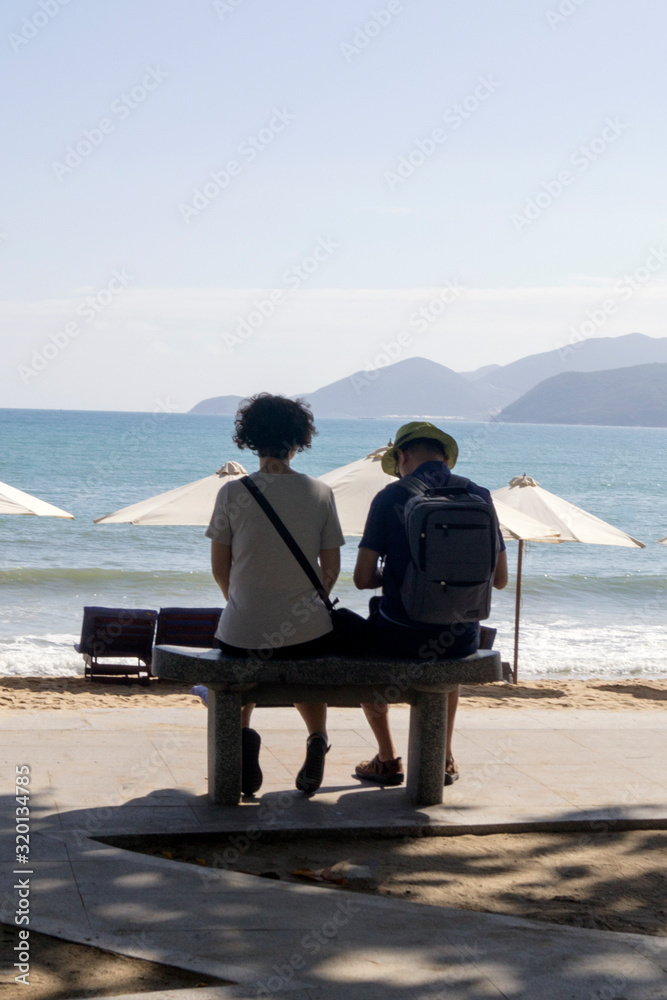 man and woman sit on a bench on the background of the beach and sea