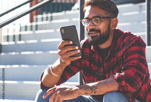Handsome young man, outdoor. Indian man is sending a voice message on a cell phone.