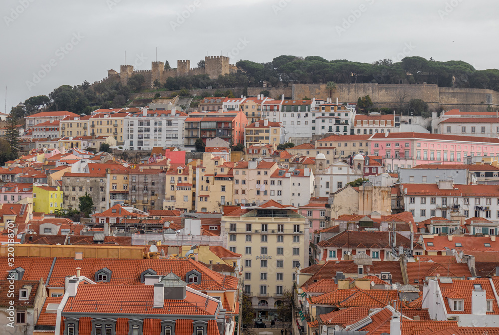 Views of the houses with tiled roofs and colorful facades in Lisbon, with the castle of San Jorge in the top of the hill