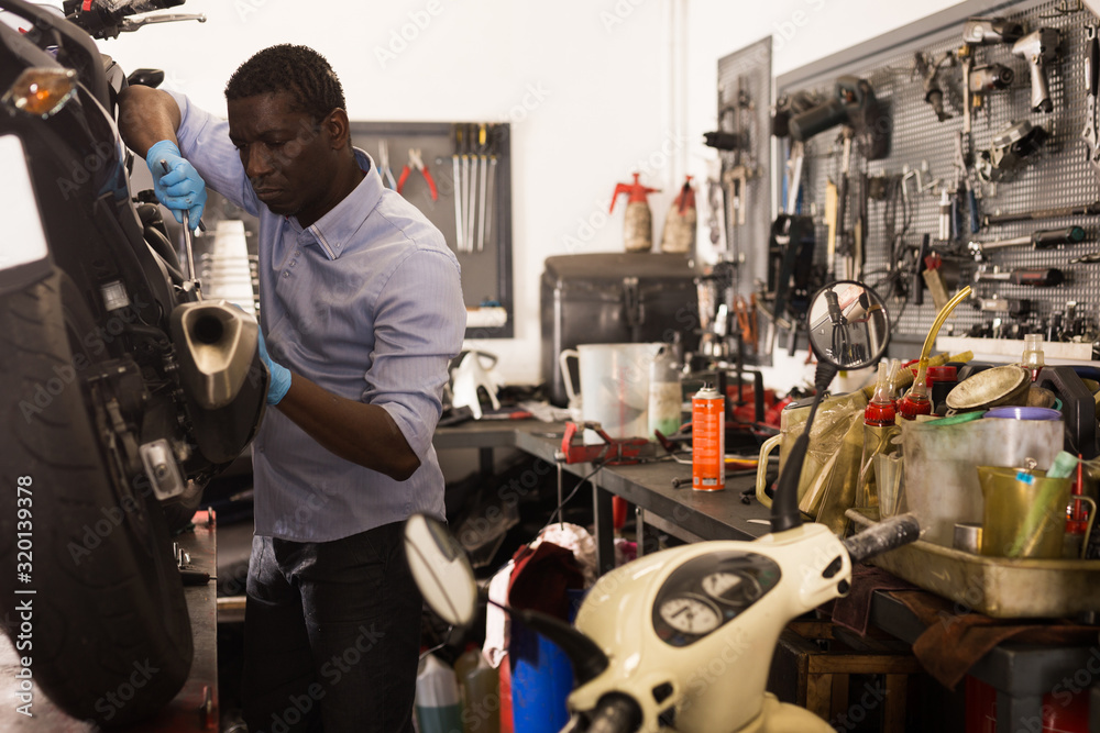 Afro american worker working at restoring motorbike in motorcycle workshop