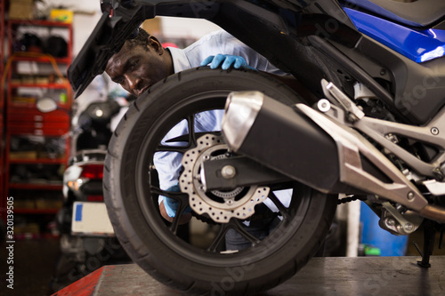 Afro american expert inspects the wheel of a motorcycle © JackF