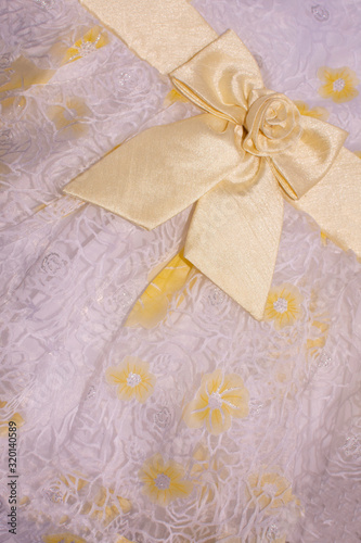 Beautiful yellow fabric bow on bright background with floral pattern. Closeup. © Ilona