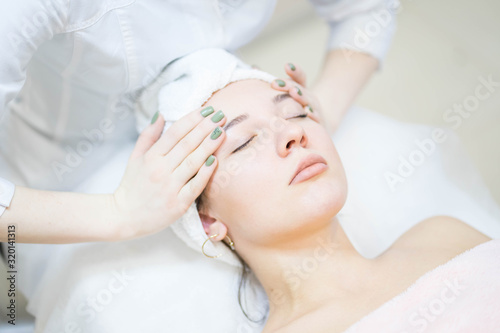 Woman in white and pink towel is having a face massage from a doctor cosmetologist in a white uniform
