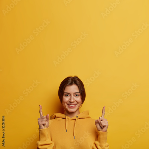 Obraz na plátně Friendly looking lovely woman shows promo with joy, points above with both index