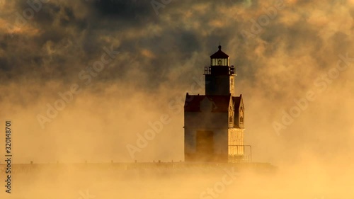 Scenic Lake Michigan lighthouse amid swirling storm of fog at sunrise on a very cold Winter day, seamless loop. photo