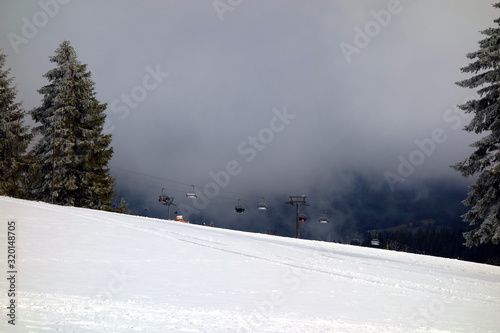 Blick auf die Skipiste am Feldberg mit Schneekanonen und Sessellift. Bewölktes, düsteres Wetter und beschneite Piste