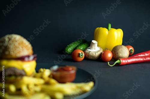 Fresh vegetables near hamburger, french fries and ketchup on black background