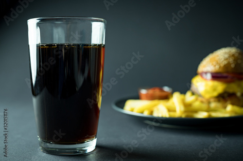 Cola in glass near blurred burger and french fries on black background 