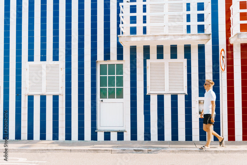 traditional and colorful houses of costa nova. young handsome man walking along street with typical striped houses in Costa Nova, Aveiro, Portugal. Fisherman's village in summer. copy space for text.