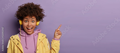 Fotografie, Obraz Millennial hipster girl with Afro hair enjoys music podcast in headphones, point