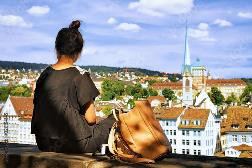 Girl sitting on Lindenhof hill and looking into Zurich, Switzerland. Limmatquai and Predigerkirche on the background.