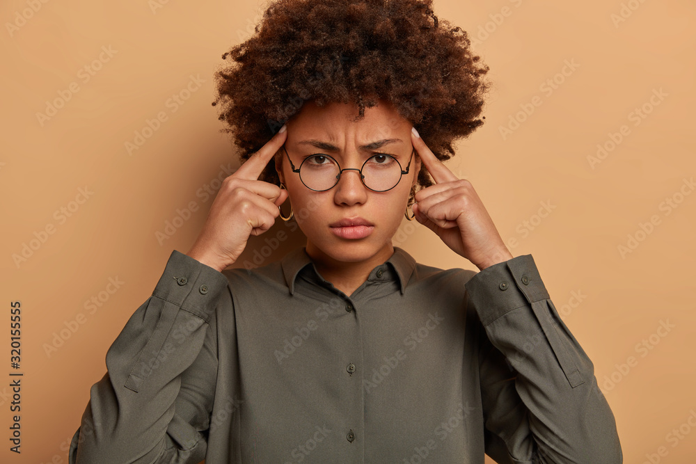 Intense displeased woman touches temples with index fingers, feels severe headache, cannot continue working, feels distressed and overworked, cant remember necessary information in noisy atmosphere Intense displeased woman touches temples with index fingers, feels severe headache, cannot continue working, feels distressed and overworked, cant remember necessary information in noisy atmosphere
