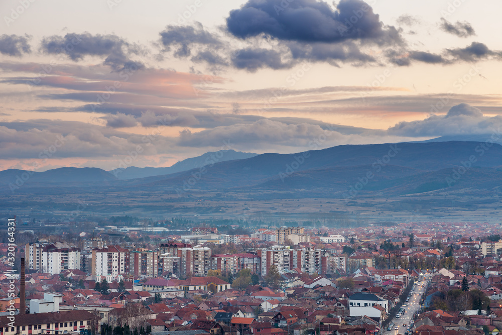 Pirot, Serbia cityscape viewed from a vantage point during a sunset with foreground buildings and city lights and distant mountain layers under colorful sky 