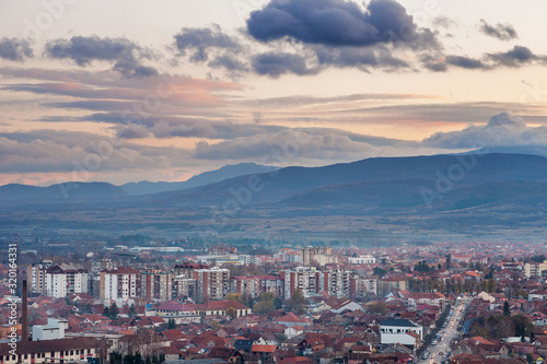 Fototapeta Naklejka Na Ścianę i Meble -  Pirot, Serbia cityscape viewed from a vantage point during a sunset with foreground buildings and city lights and distant mountain layers under colorful sky 