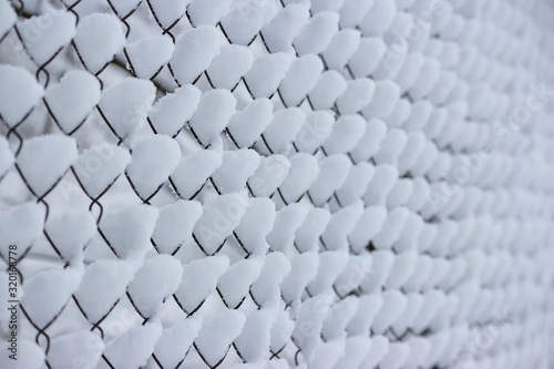 A piles of snow on the cells of the mesh fence. Snowfall in winter