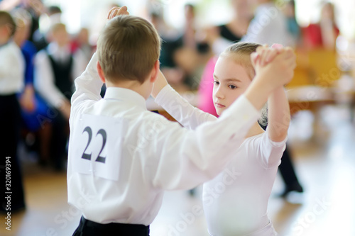 Happy young children participating in dance competition at dancing school. Boy and girl dressed in white dancing together.