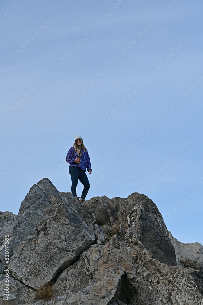 Young woman in blue sweater enjoys view of tranquil Pyramid Lake, Nevada from rock formation on coast on a calm clear winter afternoon.