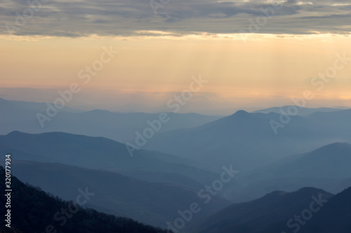 Soft, colorful view of distant mountain layers in Bulgaria from Old mountain in Serbia, lighten by morning sun rays under dramatic, vibrant sunrise sky © Nikola