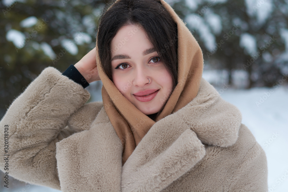 girl in a scarf on her head and in a fur coat in the winter forest