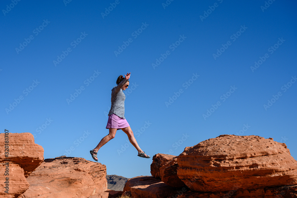 Naklejka premium Woman Jumps Over Sandstone Boulders