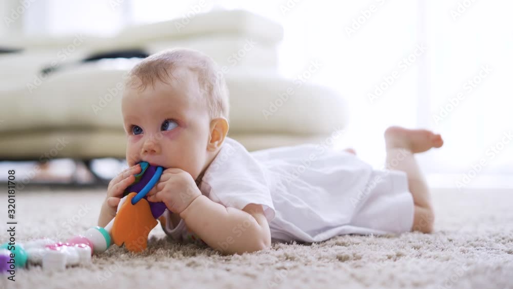 Cute baby girl playing and biting her toy while lying on the fur carpet in living room at home. Shot in 4k resolution Cute baby girl playing and biting her toy while lying on the fur carpet in living room at home. Shot in 4k resolution