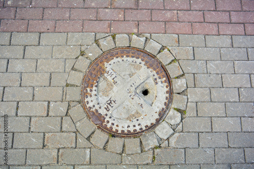Ancient cast iron rusty manhole on pavement sidewalk of city street
