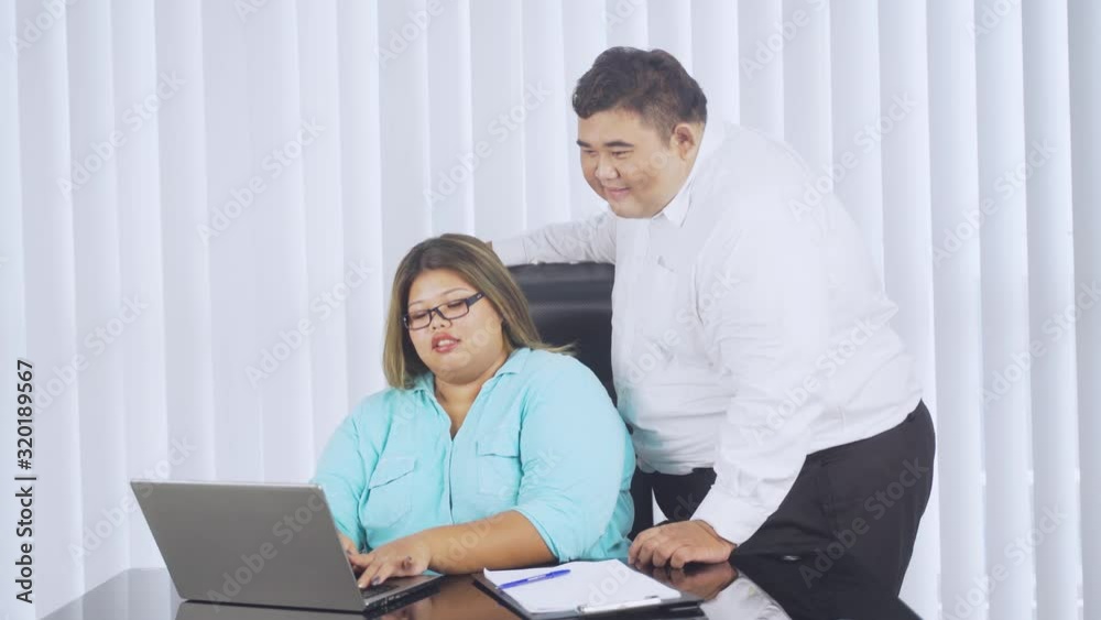 Overweight businessman giving instruction to his obese employee while pointing at screen of laptop in the office. Shot in 4k resolution Overweight businessman giving instruction to his obese employee while pointing at screen of laptop in the office. Shot in 4k resolution
