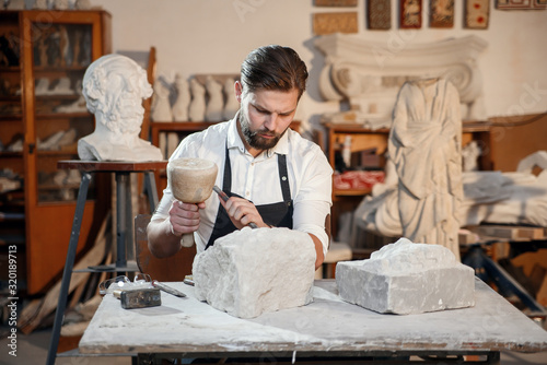 Stone carver works with wooden hammer and chisel at limestone. photo