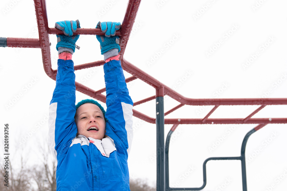 Girl hanging from the monkey bars in winter at recess Girl hanging from the monkey bars in winter at recess