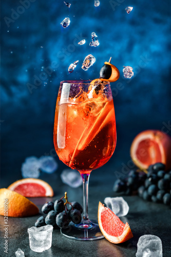 Świeży grapefruitowy koktajl z pomarańcze, winogronami i lodem w wineglass na zmroku - błękitny tło. Strzał studio napoju w zamrożonym ruchu, latający lód, krople w plusk cieczy. Letni zimny napój i koktajl