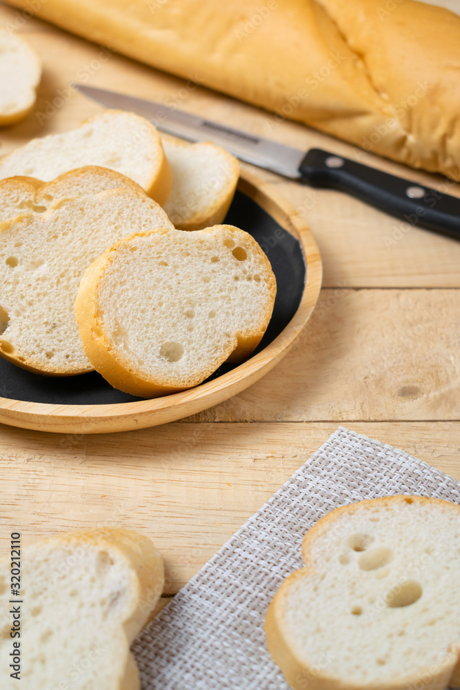 Sliced baguettes on wooden dish with knife on the wooden table.