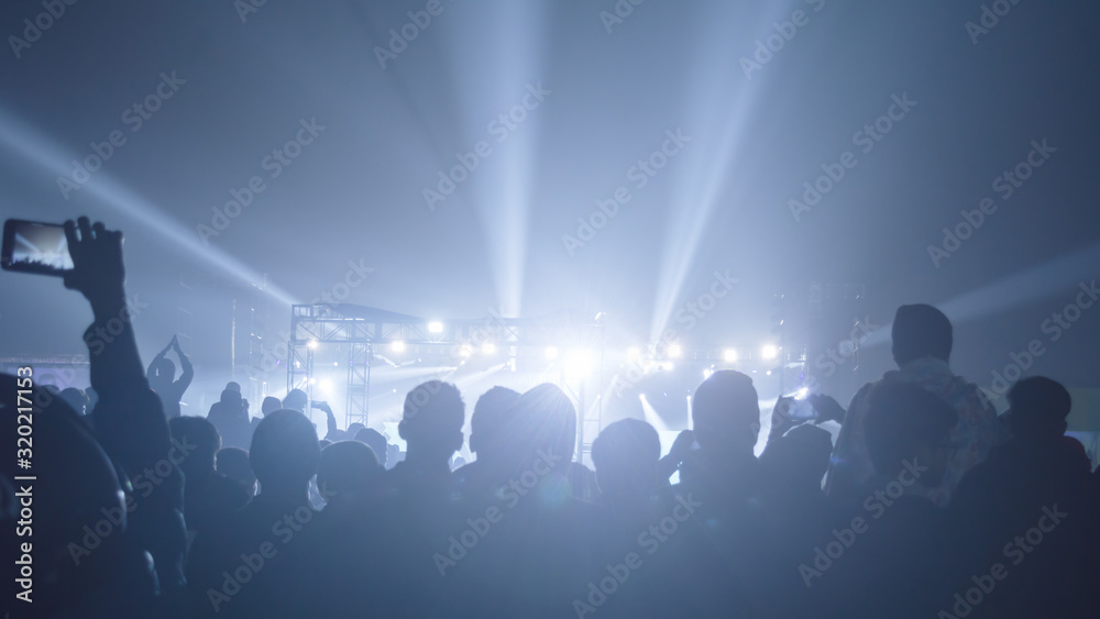 Silhouette of big audience crowd of happy people standing at concert grounds cheering clapping use smart phones raising hands up in air facing music band enjoying. Stage light reflection in front. Silhouette of big audience crowd of happy people standing at concert grounds cheering clapping use smart phones raising hands up in air facing music band enjoying. Stage light reflection in front.