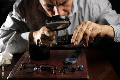 Mature man working at home as a watchmaker and jeweler composing an old clock using a screwdriver and a magnifying glass to be able to see closely