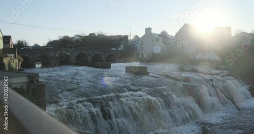 Wide shot of a broad natural waterfall with foamy water streaming over the edge and falling into the river on a beautiful sunny day. photo