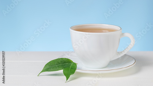 Two green leaves on a white Cup of tea on a white table.