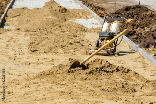 a gasoline-powered device for compacting sand and a shovel