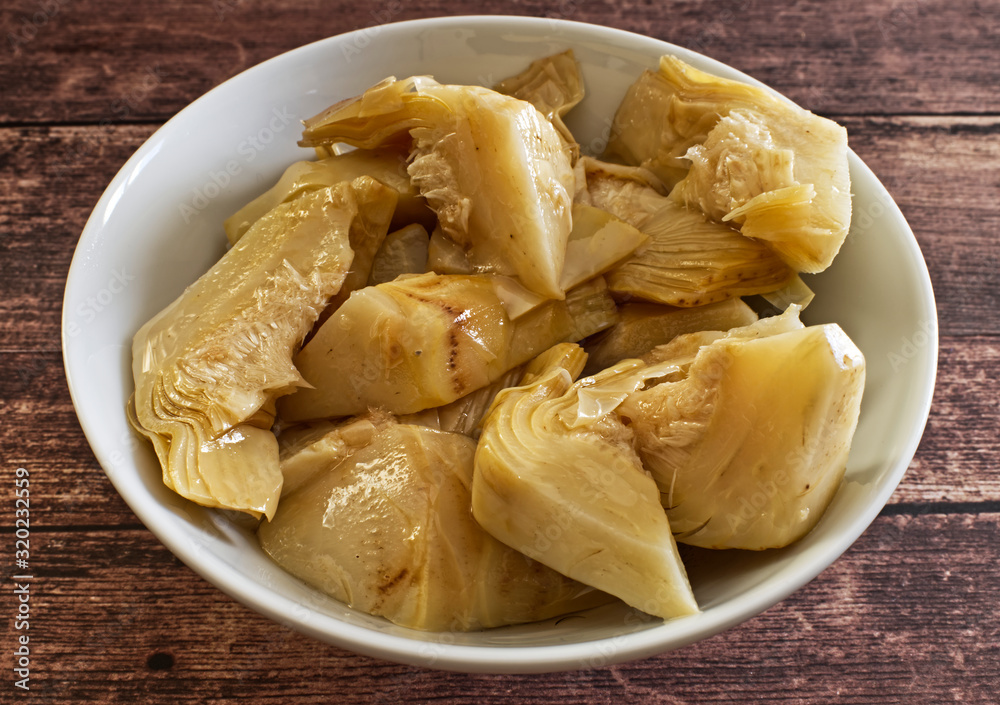 Pickled artichokes in white bowl on wooden table