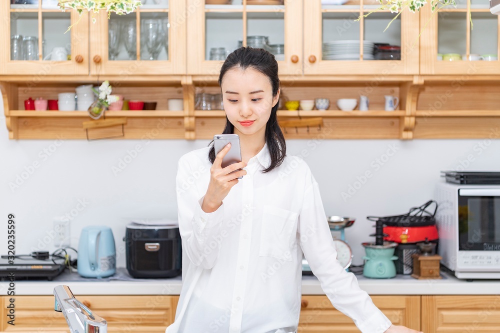 キッチンで携帯電話を操作する女性 キッチンで携帯電話を操作する女性